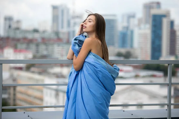 Ragazza nuda avvolta in una coperta si trova sulla terrazza con vista sulla città . — Foto Stock