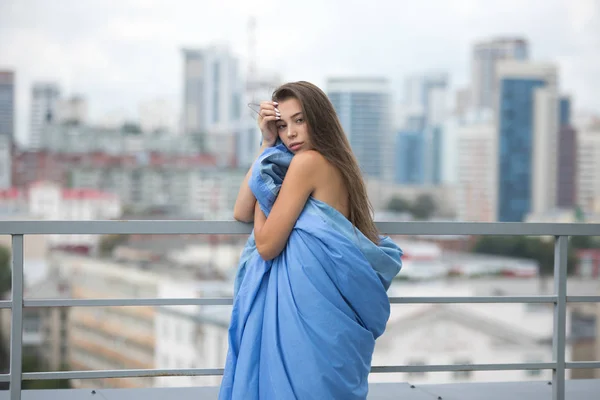 Ragazza nuda avvolta in una coperta si trova sulla terrazza con vista sulla città . — Foto Stock