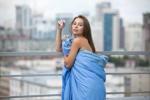 Ragazza nuda avvolta in una coperta si trova sulla terrazza con vista sulla città . — Foto Stock