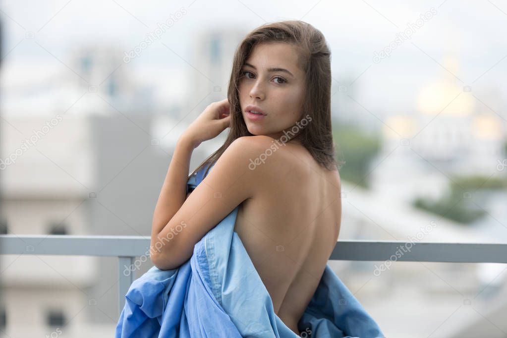 Naked girl wrapped in a blanket stands on the terrace overlooking the city.