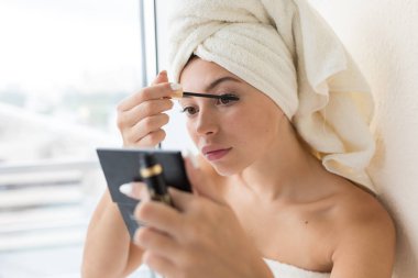 Başında beyaz havlu ile güzel kadın makyaj yapar .