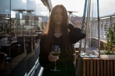 Genç kadın bir kadeh şarap ile bir restoranın terasında duruyor.