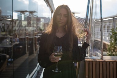 Genç kadın bir kadeh şarap ile bir restoranın terasında duruyor.