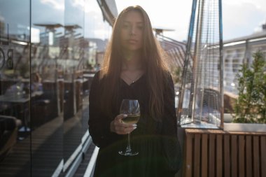 Genç kadın bir kadeh şarap ile bir restoranın terasında duruyor.