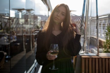 Genç kadın bir kadeh şarap ile bir restoranın terasında duruyor.