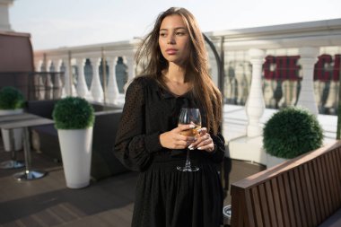 Genç kadın bir kadeh şarap ile bir restoranın terasında duruyor.