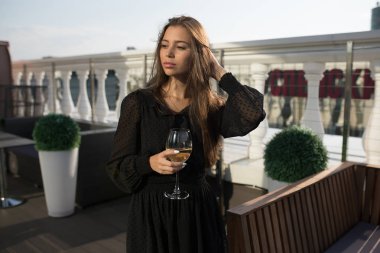 Genç kadın bir kadeh şarap ile bir restoranın terasında duruyor.