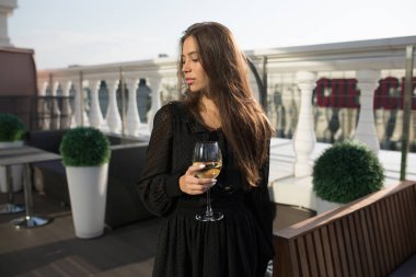 Genç kadın bir kadeh şarap ile bir restoranın terasında duruyor.