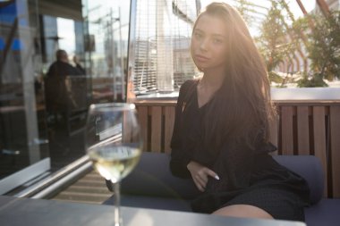 Genç kadın bir masada bir restoran terasında bir kadeh şarap ile oturuyor..