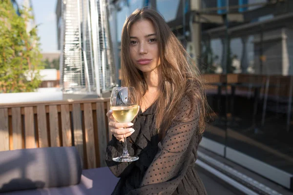 Bir kadeh şarap ile bir restoranın terasında oturan genç kadın.