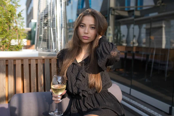 Jonge vrouw zittend op het terras van een restaurant met een glas wijn. — Stockfoto