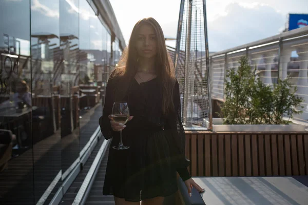 Молодая женщина стоит на террасе ресторана с бокалом вина . — стоковое фото