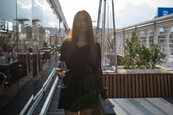 Молодая женщина стоит на террасе ресторана с бокалом вина . — стоковое фото