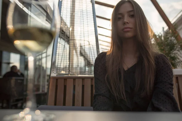 Mujer joven sentada en una mesa en la terraza de un restaurante con una copa de vino . — Foto de Stock