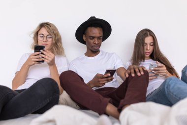 Arkadaşlar çok ırklı grup üzerinde yatak ve usie smartphone oturuyor.