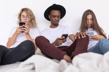 Arkadaşlar çok ırklı grup üzerinde yatak ve usie smartphone oturuyor.