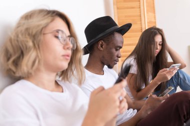 Arkadaşlar çok ırklı grup üzerinde yatak ve usie smartphone oturuyor.