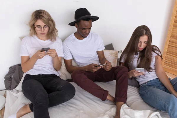 Мультирасовая группа друзей сидит на кровати и пользуется смартфоном . — стоковое фото