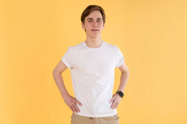 Ung man i en vit t-shirt står på gul bakgrund. Mock-up. — Stockfoto