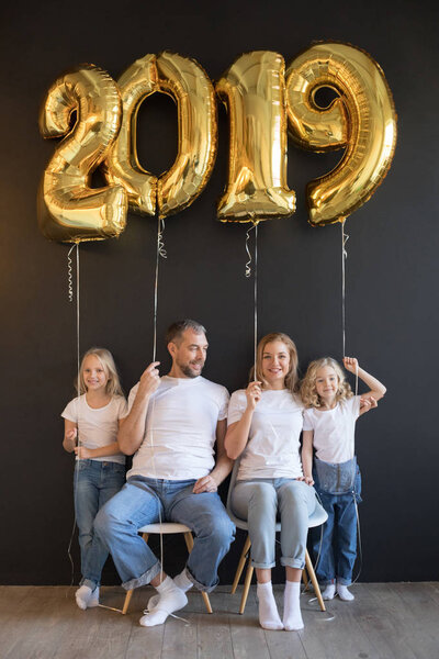 Happy family holding sign 2019 made of golden balloons for new year on black background.