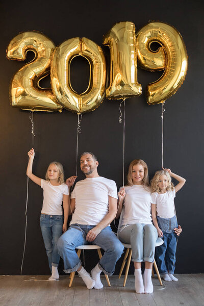Happy family holding sign 2019 made of golden balloons for new year on black background.