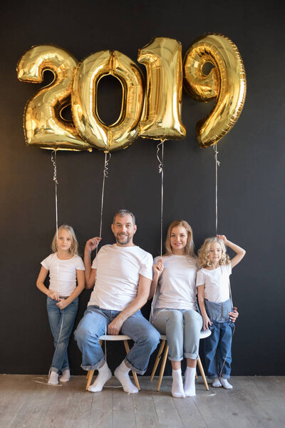 Happy family holding sign 2019 made of golden balloons for new year on black background.