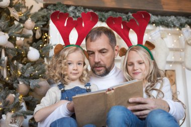 Baba kız Noel ağacı yakınındaki bir kitap okur..