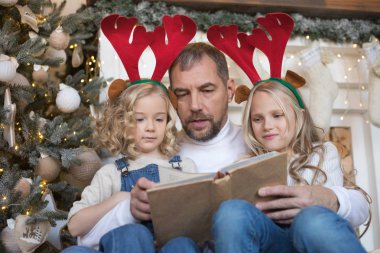 Baba kız Noel ağacı yakınındaki bir kitap okur..