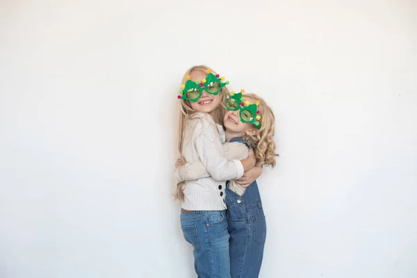 Two little girls hugging in funny glasses in the form of Christmas trees. — Stock Photo, Image