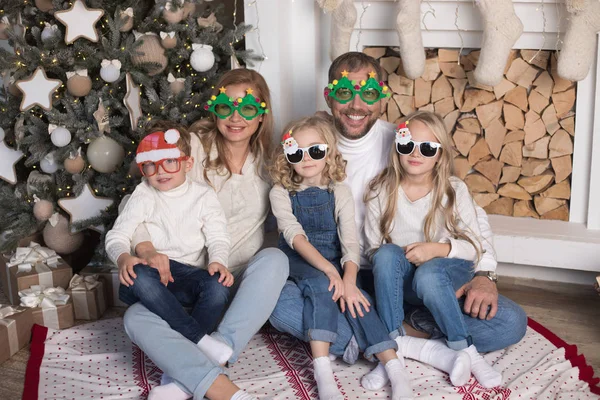 Joyeux famille assis près du sapin de Noël dans des lunettes drôles . — Photo