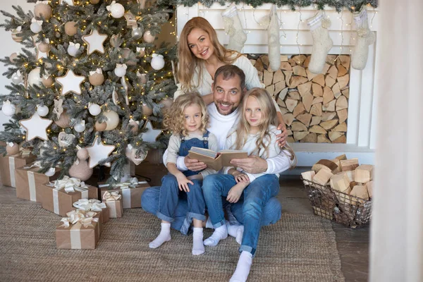 Joyeux famille assise près du sapin de Noël et lisant un livre . — Photo