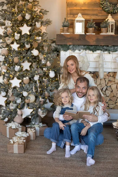 Glückliche Familie sitzt am Weihnachtsbaum und liest ein Buch. — Stockfoto