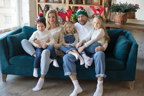 Joyeux famille dans des chapeaux de Noël drôles assis sur le canapé . — Photo