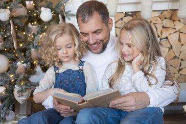 Baba kız Noel ağacı yakınındaki bir kitap okur..