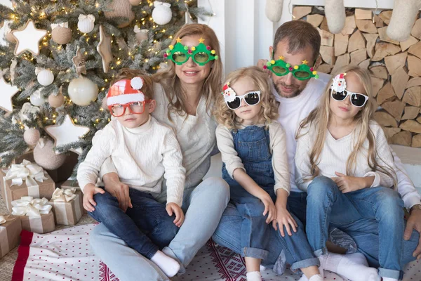 Joyeux famille assis près du sapin de Noël dans des lunettes drôles . — Photo
