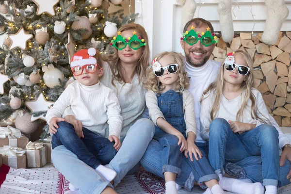 Joyeux famille assis près du sapin de Noël dans des lunettes drôles . — Photo