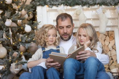 Baba kız Noel ağacı yakınındaki bir kitap okur..