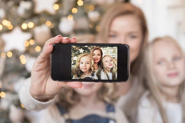 Mother make selfie with her daughters on the background of the Christmas tree.