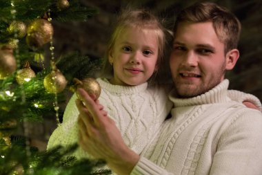 Baba kızın kollarında tutar ve Noel ağacı süsleyin.