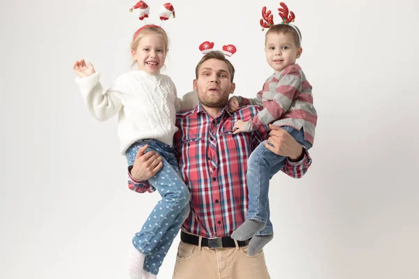 Père tient des enfants dans ses bras sur un fond blanc. Joyeux famille dans les bandeaux de Noël drôles . — Photo