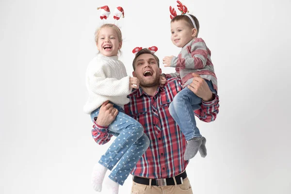 Père tient des enfants dans ses bras sur un fond blanc. Joyeux famille dans les bandeaux de Noël drôles . — Photo