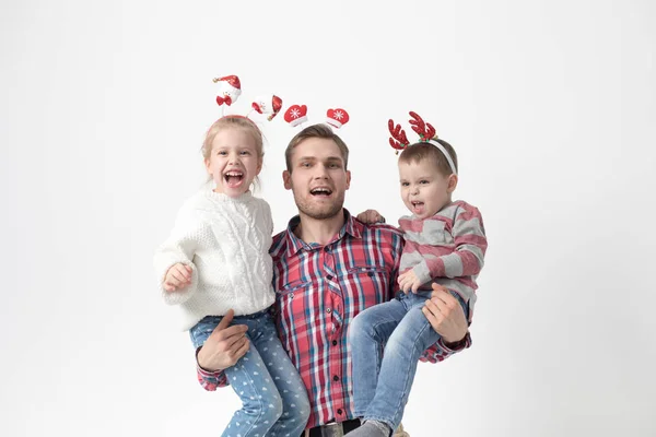 Far håller barn i famnen på en vit bakgrund. Lycklig familj i roliga jul pannband. — Stockfoto