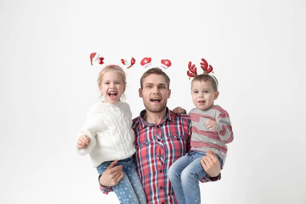 Far håller barn i famnen på en vit bakgrund. Lycklig familj i roliga jul pannband. — Stockfoto