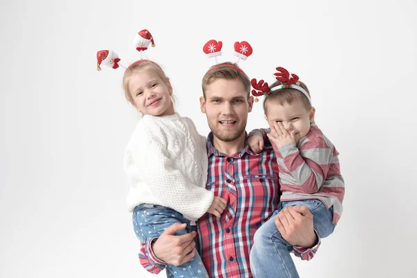 Far håller barn i famnen på en vit bakgrund. Lycklig familj i roliga jul pannband. — Stockfoto