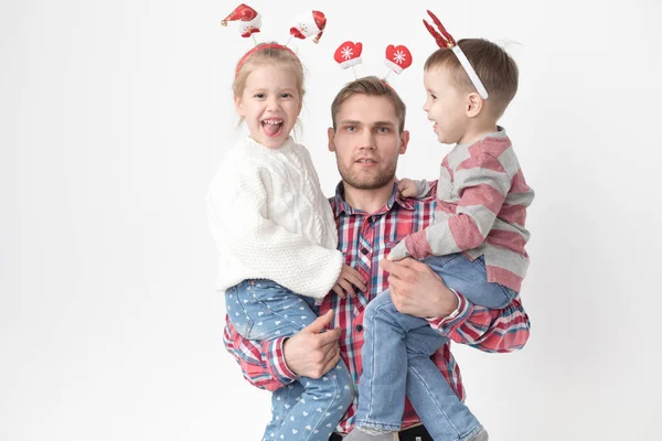 Far håller barn i famnen på en vit bakgrund. Lycklig familj i roliga jul pannband. — Stockfoto