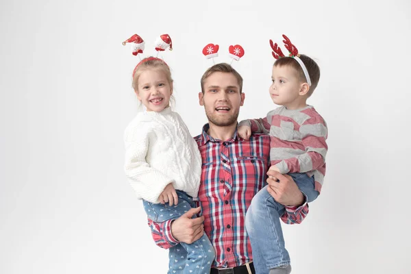 Far håller barn i famnen på en vit bakgrund. Lycklig familj i roliga jul pannband. — Stockfoto