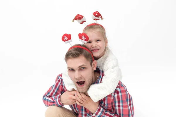 En liten flicka sitter på sina fäder tillbaka. Familj i roliga jul pannband på vit bakgrund. — Stockfoto