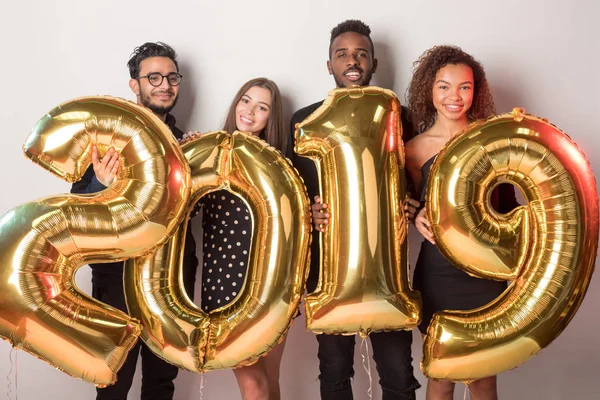 Young company of friends holding sign 2019 made of golden balloons for new year on white background.