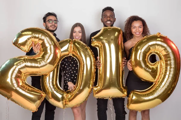 Joven compañía de amigos sosteniendo cartel 2019 hecho de globos de oro para el nuevo año sobre fondo blanco . — Foto de Stock