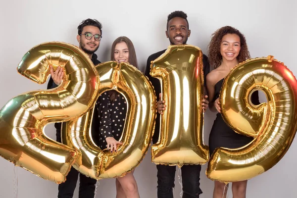 Joven compañía de amigos sosteniendo cartel 2019 hecho de globos de oro para el nuevo año sobre fondo blanco . — Foto de Stock